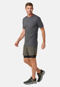 Camiseta de manga corta gris oscuro, pantalones cortos livianos color verde olivo y zapatillas deportivas negras con detalles grises. Diseño simple, ajuste casual.