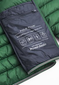 Grön puffjacka med en mörkgrå innerfoder, utrustad med en dragkedjeficka och tryckta skötselsymboler med en randig nederkant.