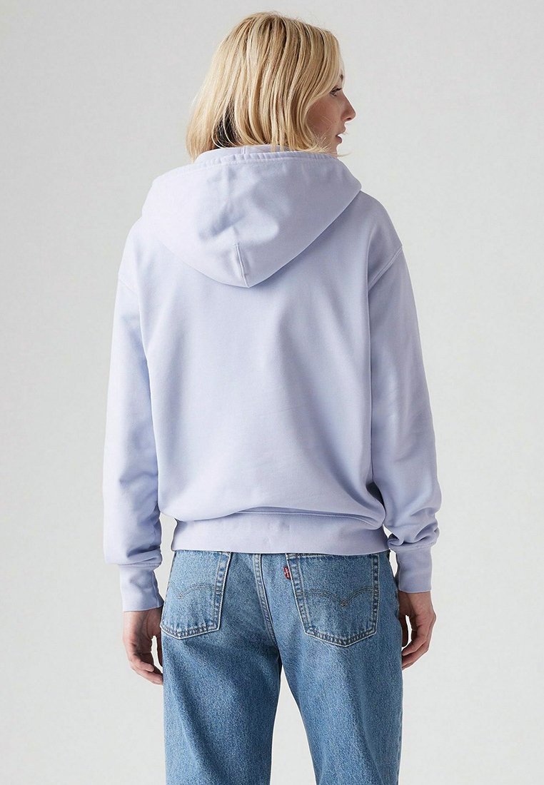 Felpa di cotone viola chiaro con cappuccio regolabile, texture morbida e vestibilità rilassata, abbinata a jeans in denim azzurro.