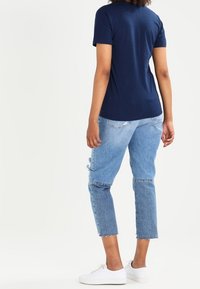 Námořnická modrá tričko s krátkými rukávy, spárované se světle modrými džíny s opotřebeným vzhledem. Džíny mají zkrácený, třepený lem a opotřebované akcenty.