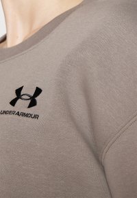 Šedá mikina vyrobená z měkké látky, se zaobleným výstřihem, žebrovanými manžetami a vyšitým černým logem Under Armour na hrudi.