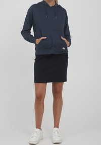 Marinblå hoodie med en stor framficka, kombinerad med en marinblå pennkjol. Modellen har vita sneakers. Slätt tyg, avslappnad design.