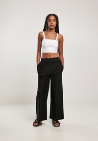 Top court blanc à bretelles larges, associé à un pantalon ample noir à côtes avec poches latérales. Des sandales noires complètent le look.