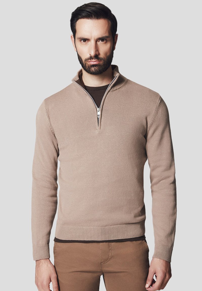 Beżowy sweter dzianinowy z kołnierzem na ćwierć zamka, prążkowanymi mankietami i dołem oraz gładką teksturą. Nosi się go na ciemno-brązowej koszuli.