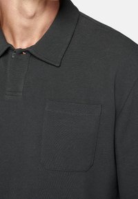 Tmavě šedá polo košile s texturovanou tkaninou, s překládaným límcem a jednou náprsní kapsou. Obsahuje zapínání na knoflíky a čisté šití.