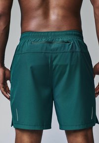 Mørkegrønne sports-shorts lavet af letvægtsstof. Har en elastisk talje, sidelommer og reflekterende detaljer.