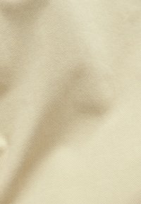 Beige gestructureerde stof met een fijne geribbelde patroon, met lichte kreukels, die duidt op een zachte, middelzware kwaliteit.