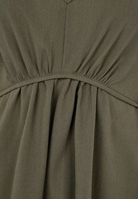 Robe vert olive avec une jupe plissée et une taille froncée, fabriquée dans un tissu léger au toucher doux. Design en V.