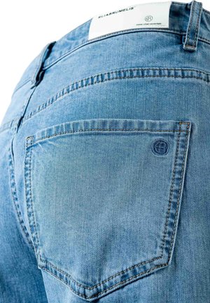 Primo piano della tasca posteriore di jeans in denim azzurro con cuciture marroni e un'etichetta bianca in vita.