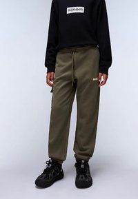 Pantalones jogger verde oliva con piernas estrechas, cintura elástica y cordón negro. Combinados con una camiseta negra de manga larga con un logo gráfico.