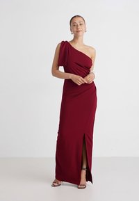 Burgunderfarget en-skulderkjole laget av glatt stoff, med en thigh-high splitt og drapert design. Enkel og elegant med minimale detaljer.