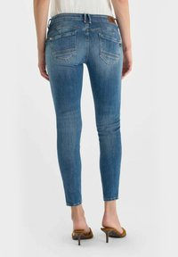 Strakke blauwe spijkerbroek met een vervaagde finish, voorzien van een taille met middelhoge taille, twee achterzakken en minimale stiksel details.