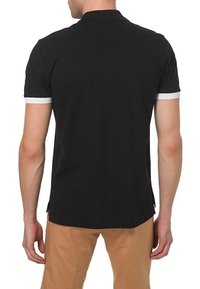 Polo noir avec un col à bords blancs, manches courtes et ourlet droit. Présente des fentes sur les côtés pour faciliter les mouvements.