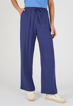 Person wearing loose, navy blue textured pants with elastic waistband and drawstring, paired with white low-top sneakers.