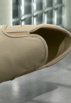 Smėlio spalvos slip-on batai su minkšta audinio tekstūra, apvalia forma ir minimaliais siūlėmis. Vidaus dalis lygi ir paprasta, pasižyminti minimalistiniu dizainu.