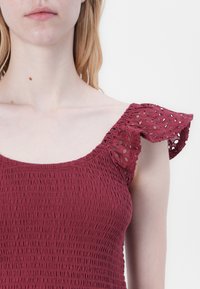 Raspberry-colored top with smocked texture, featuring ruffled sleeves with cut-out detailing, made from lightweight fabric.