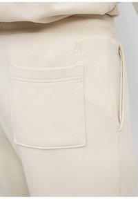 Beige sweatpants met een rechthoekige achterzak. Zacht materiaal en een subtiele geborduurde logo-detail nabij de tailleband.