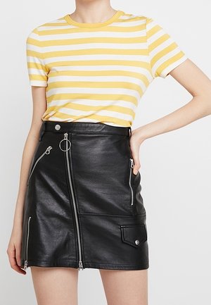 Mujer con top de manga corta a rayas amarillas y blancas, metido en una minifalda de cuero negro con múltiples cremalleras y un bolsillo.