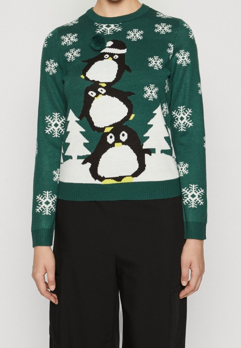 Pull en tricot vert avec un motif de pingouin, orné de flocons de neige blancs et d'arbres. Poignets et ourlet côtelés. Pompom décoratif sur le pingouin du haut.