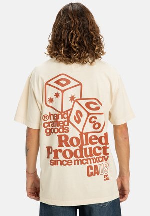 Camiseta beige con gran diseño gráfico marrón con texto y cubos en la parte posterior. Mangas cortas y ajuste relajado. Material de algodón.