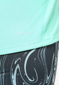 Camiseta atlética verde menta con un tejido de malla texturizado y logo "DRI-FIT". Combinada con leggins oscuros que presentan un patrón gris en espiral.