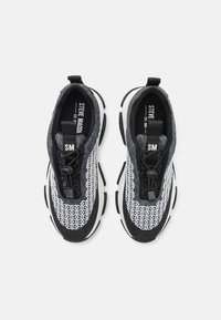 Černobílé tenisky s horní částí z prodyšné síťoviny s geometrickým vzorem, výraznými tkaničkami a polstrovanou podešví pro pohodlí.