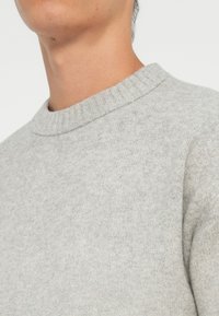 Gray knit sweater featuring a ribbed crew neckline, soft texture, and a fitted design, suitable for casual wear.