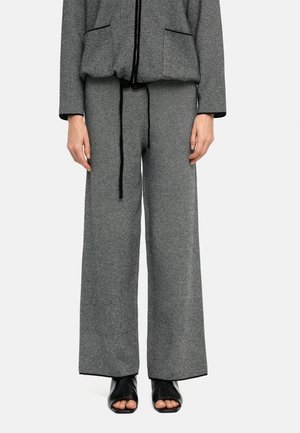 Szare spodnie z szerokimi nogawkami z czarnym bocznym paskiem, w zestawie z pasującą marynarką i czarnymi sandałami na obcasie z odsłoniętymi palcami.