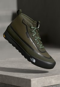 Grønn høy-top sneaker med en teksturert overdel, gummisåle, snøring og logo på siden. Har et elegant, moderne design.