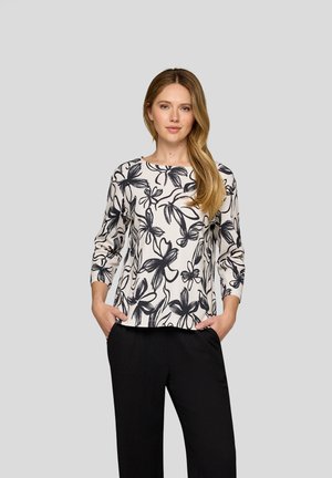 Langärmlige Bluse mit weißem Hintergrund und schwarzen Blumenmustern, ergänzt durch einen runden Ausschnitt und eine lockere Passform.