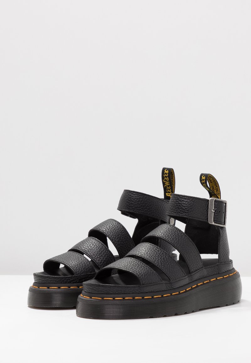 Black leather sandals with wide cross straps, adjustable ankle buckle, textured surface, and a thick black platform sole with orange stitching.