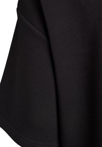 Čierna bavlnená látka s hladkou textúrou, s rozšíreným strihom. Obsahuje bočnú kapsu a prešívaný lem, ktorý ukazuje jednoduchosť v štýle.