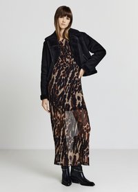 Cappotto in shearling nero sopra un vestito con stampa leopardata e uno strato trasparente. Stivaletti neri con un lieve tacco completano l'outfit.