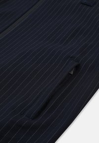 Chaqueta de tela azul marino con rayas verticales en azul claro; presenta un cierre frontal con cremallera y un bolsillo lateral con cremallera oculta.