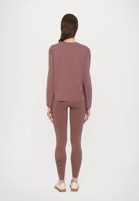 Mauve gara piedurkne krekls, kas saskaņots ar atbilstošām legingām, abi izgatavoti no mīksta auduma. Legingām ir logo apdruka malā. Vienkāršs, pieguļošs dizains.
