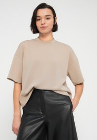 Μπεζ κοντομάνικη μπλούζα με ψηλό λαιμό, άνετη εφαρμογή και απαλή υφή, σε συνδυασμό με μαύρο δερμάτινο παντελόνι ψηλόμεσο.