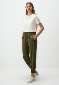 Witte T-shirt met korte mouwen, gecombineerd met groene joggingsbroeken met elastische taille, zijzakken, elastische boorden en een gladde textuur. Witte sneakers.