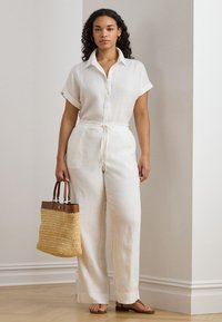 Balts linu divdaļīgs apģērbs ar apkaklīti, īsām piedurknēm un plašām biksēm. Komplektā austs salmu soma.