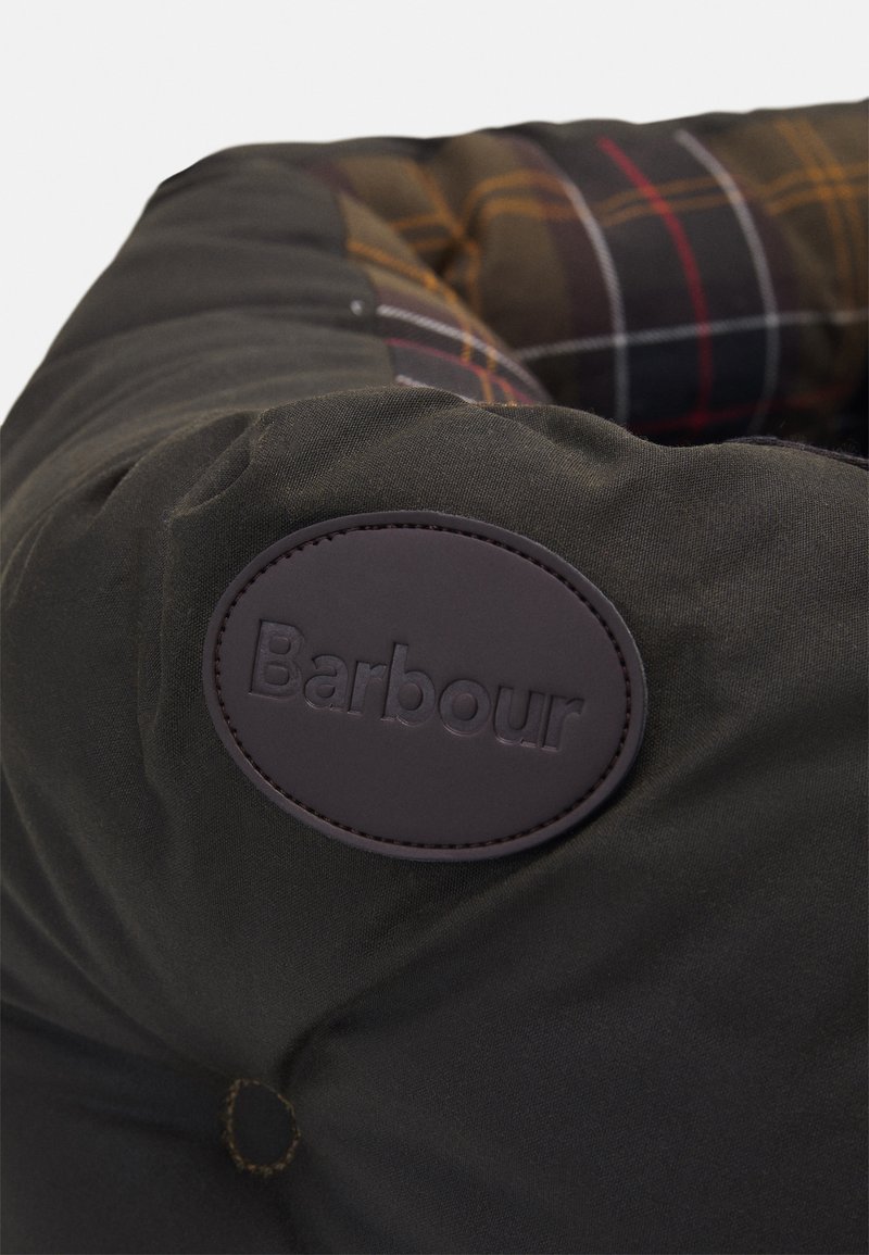 Cama para mascotas de color verde oscuro con un patrón acolchado y una etiqueta de cuero marrón. Tiene forma redonda, detalles en botones y un forro a rayas en contraste.