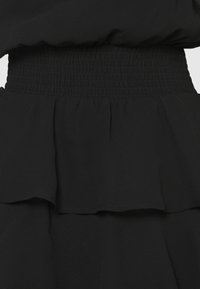 Svart plagg med bred, rynkad midjeband och lager av löst tyg under midjan, som visar textur och sömdetaljer.