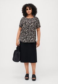 T-shirt à manches courtes avec un imprimé animal noir et beige, associé à une jupe midi noire ajustée. Les accessoires comprennent un sac noir et des sandales à plateforme.