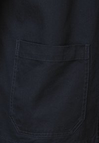 Mörkblått tyg med en slät yta, prytt med en sydd ficka på vänster sida och rena, raka linjer.