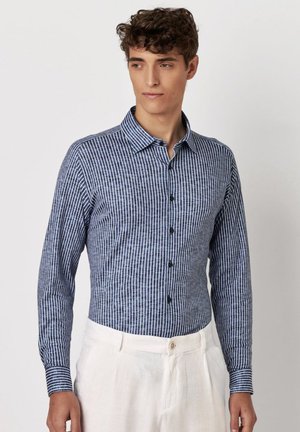 Langarmshirt met een blauw-witte gestreepte patroon, knoopsluiting aan de voorkant en een kraag. Gemaakt van een lichte stof, gecombineerd met lichte broek.
