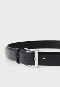 Marineblå lærbelte med en glatt overflate, med en sølvfarget metallspenne og klassisk prong-design, med flere justeringshull.