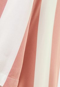 Maglietta a righe con ampie strisce rosa e bianche, realizzata in morbido tessuto di cotone. La texture appare liscia con un collo a giro standard.