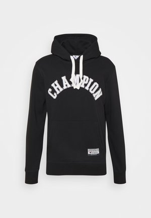 Czarna bluza z kapturem z białymi sznurkami, z tekstem "CHAMPION" wygiętym na przodzie oraz małą prostokątną metką blisko dolnego brzegu.