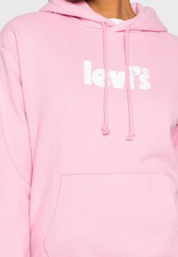Felpa cappuccio rosa chiaro con tasca frontale e logo "levi's" stampato in bianco, con due cordini pendenti dal cappuccio.