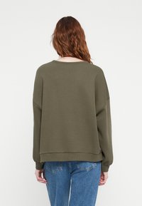 Olive green sweatshirt with a relaxed design, round neckline, and dropped shoulders. Textured fabric with ribbed cuffs and hem.