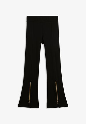 Leggings negras con parte inferior acampanada, con una cinturilla ancha y cremalleras doradas en el tobillo para mayor detalle. Tela lisa y elástica.