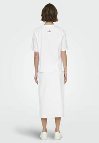 Witte t-shirt met korte mouwen en ronde hals, voorzien van een achterzijde graphic, gecombineerd met een witte rok tot de knie en witte sneakers. Zachte textuur.